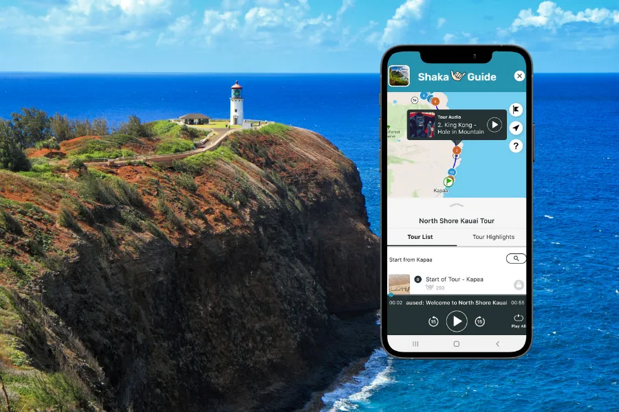 Smartphone displaying the Shaka Guide app over a dramatic ocean cliff with a lighthouse perched on the grassy headland above deep blue water.