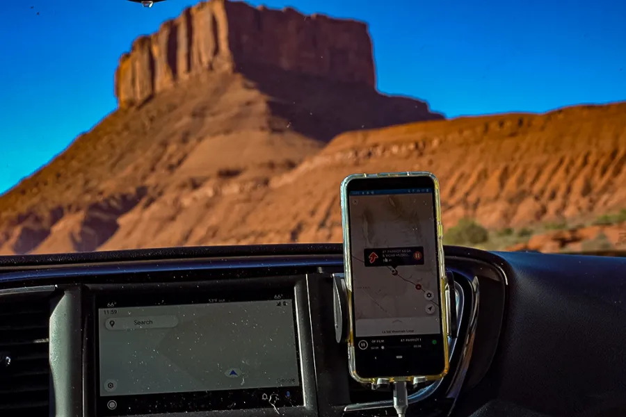 Smartphone navigation app mounted inside a car with a towering red rock desert butte visible through the windshield.