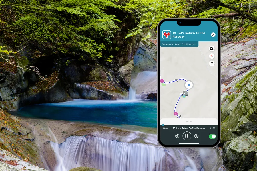 Smartphone displaying the Shaka Guide app over a turquoise forest pool with cascading waterfalls and smooth mossy rock walls.