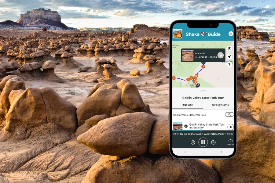 Smartphone displaying the Shaka Guide app over Goblin Valley’s strange mushroom-shaped rock formations in a wide desert landscape.