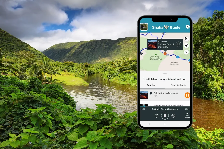 Smartphone displaying the Shaka Guide app over a lush tropical valley with a calm river, dense greenery, and steep mountains in the background.