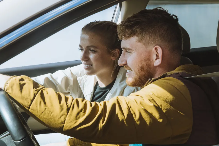 Two travelers smile together inside a car, enjoying the drive from the front seats.