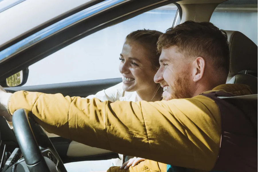 Two travelers smile inside a car, enjoying the ride together from the front seats.