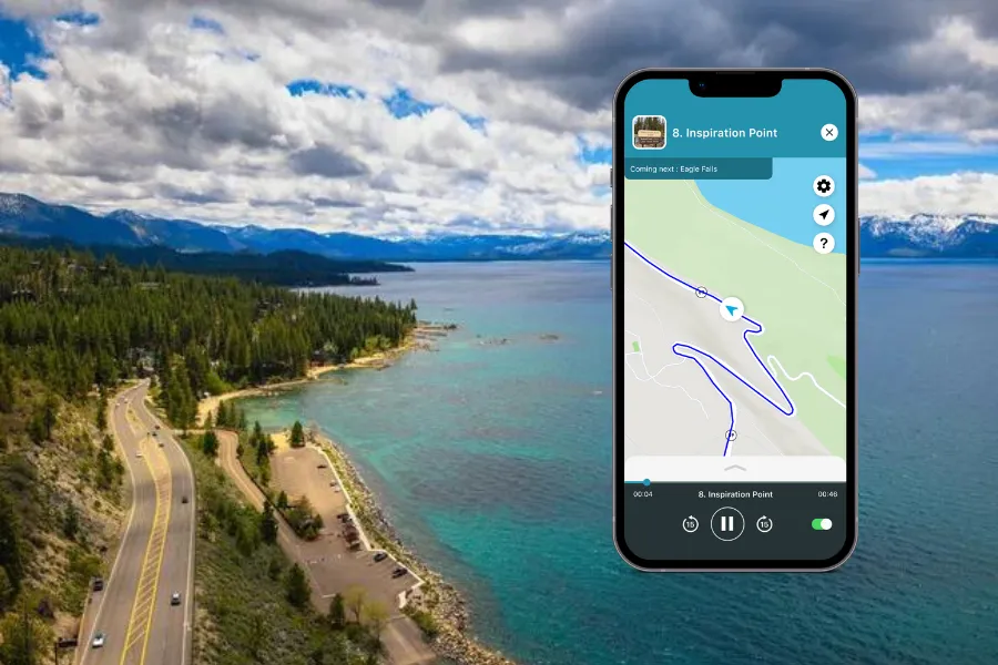 Smartphone displaying the Shaka Guide app over a scenic lakeshore with turquoise water, pine forests, mountain views, and a winding road.