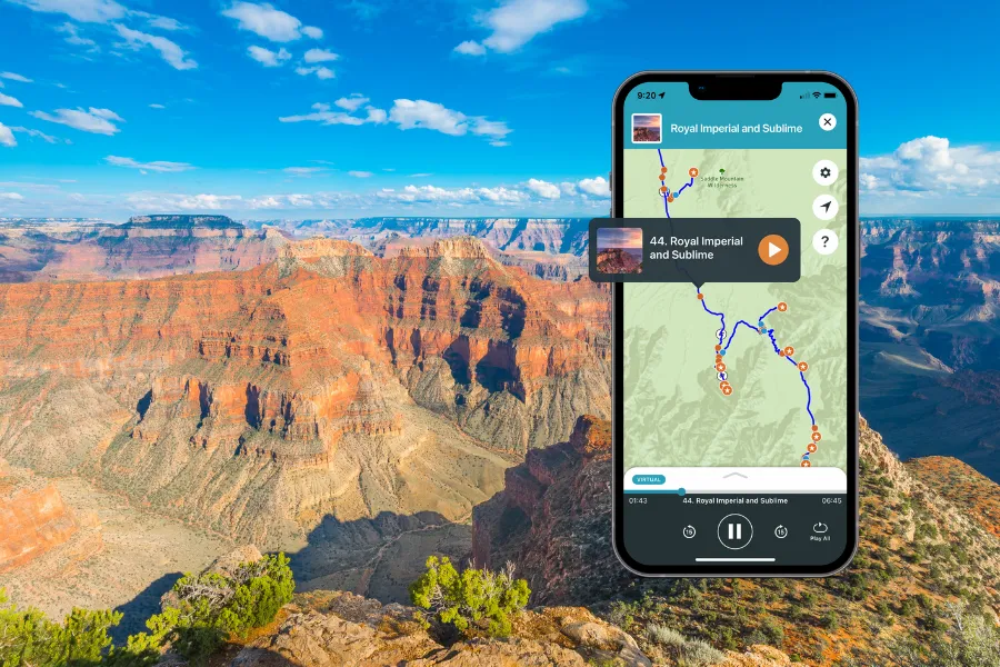 Smartphone displaying a tour app over a sweeping Grand Canyon overlook with layered red cliffs, deep canyon shadows, and a bright blue sky.