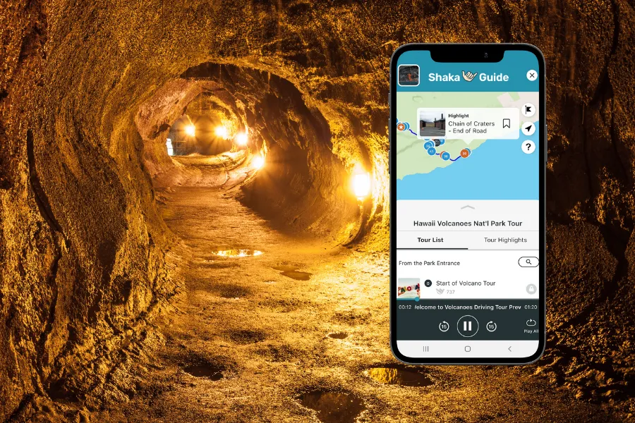Smartphone displaying the Shaka Guide app over a warmly lit lava tube tunnel with glowing lights, rough rock walls, and a winding underground path.