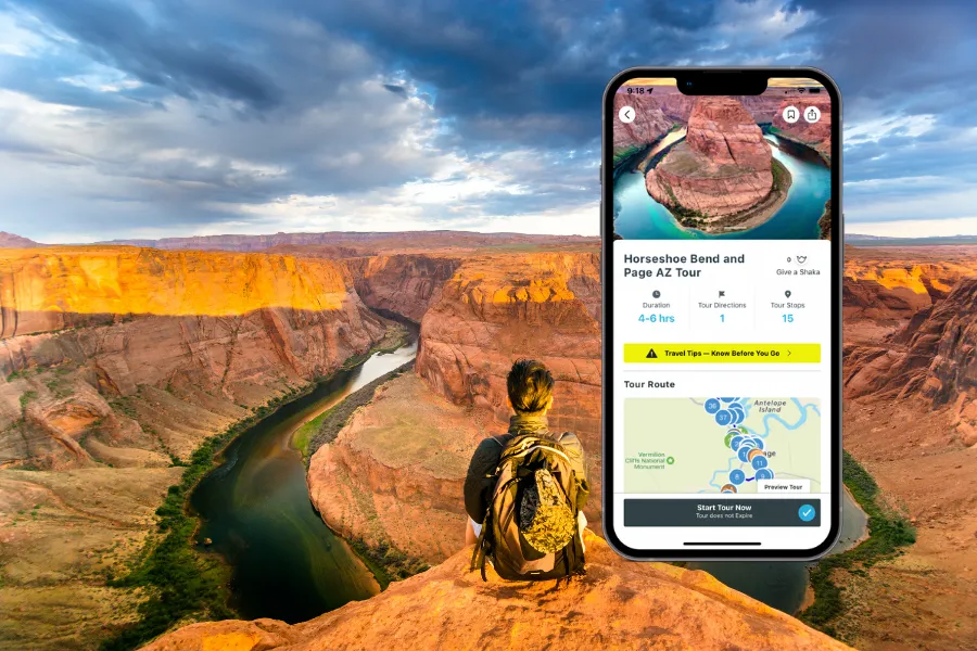 Smartphone displaying a tour app beside Horseshoe Bend, with a hiker overlooking the winding river and glowing canyon walls under dramatic clouds.