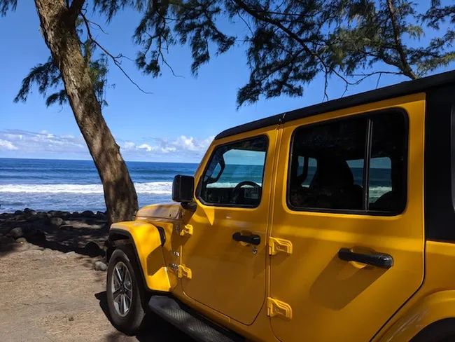 Yellow Jeep parked under a tree with ocean waves and blue sky in the background.