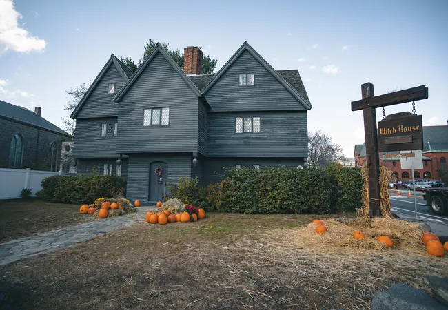 Front view of a dark wooden house decorated with pumpkins and hay for Halloween, promoting a haunted Salem witch trials and ghosts tou