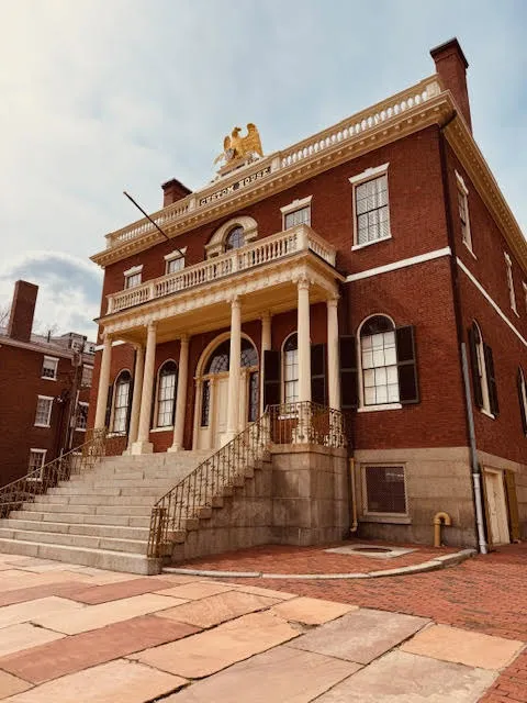 Grand historic brick building with tall white columns, wide stone steps, and a golden eagle statue on the roof.