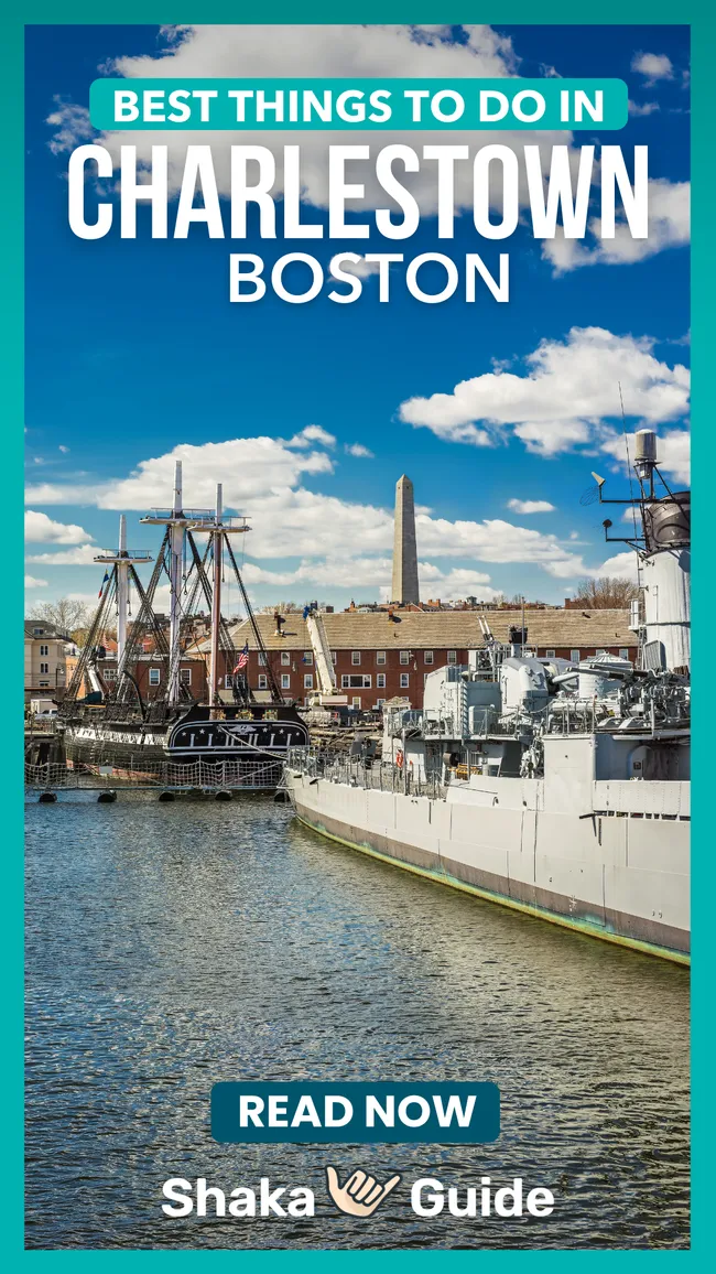 Historic harbor with docked ships, red-brick buildings, and a tall monument in the background under a blue sky.