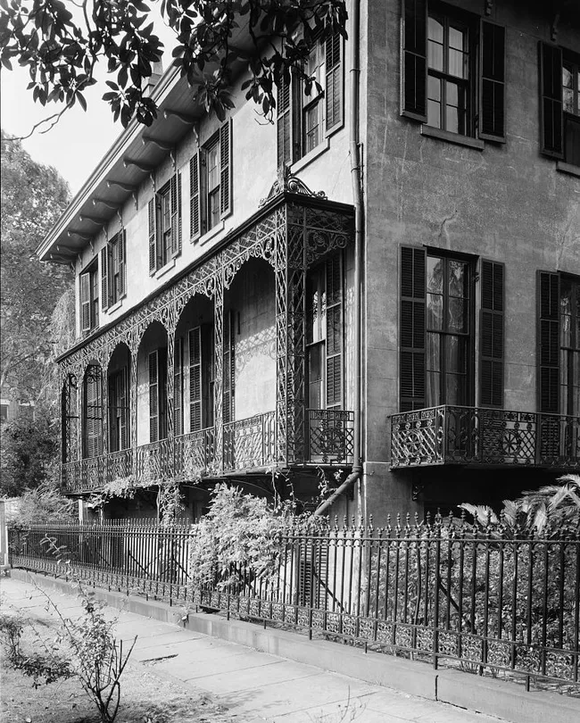 Victorian-era architecture of the Andrew-Low House, showcasing intricate ironwork on balconies and a fenced garden in Savannah, Georgia.