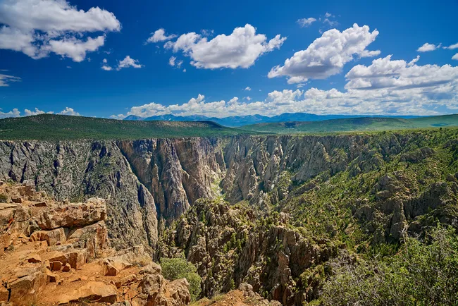 Expansive view from Warner Point showcasing the dramatic cliffs and rugged terrain of Black Canyon of the Gunnison under a bright blue sky.