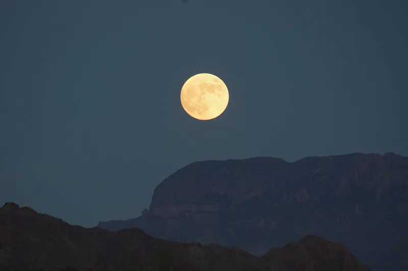 A bright full moon rises over the silhouette of desert mountains in Terlingua, Texas, under a clear night sky.