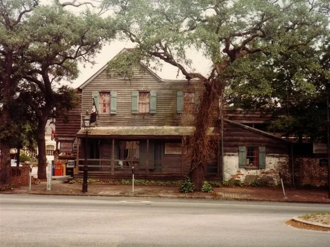 Historic wooden building with green shutters, surrounded by trees, likely representing The Pirate's House in Savannah, Georgia.