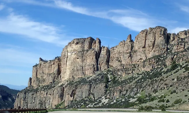 A stunning cliffside view along the road in Bighorn Canyon, Wyoming, with towering sandstone formations rising above the winding route under a clear blue sky.