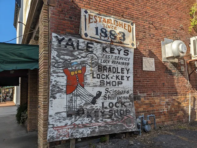 Sign on a brick wall advertising Bradley Lock and Key Shop, established in 1883, with services for locks and scissors.