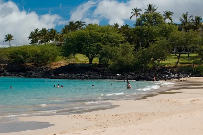 People swim and relax at Hapuna Beach, known for its soft white sand and turquoise water.