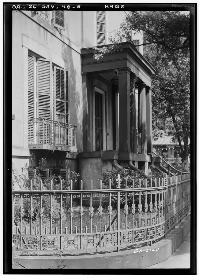 Historic architecture of the Sorrel-Weed House, featuring a wrought iron fence and front porch in Savannah.