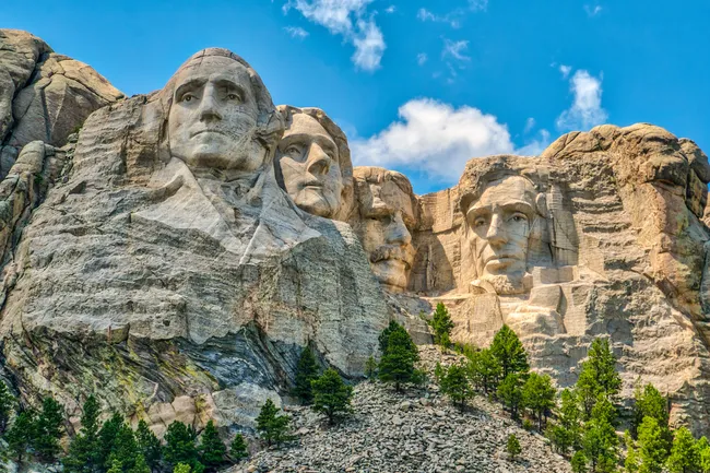 Mount Rushmore National Monument featuring the carved faces of four U.S. presidents against a blue sky and rocky background.