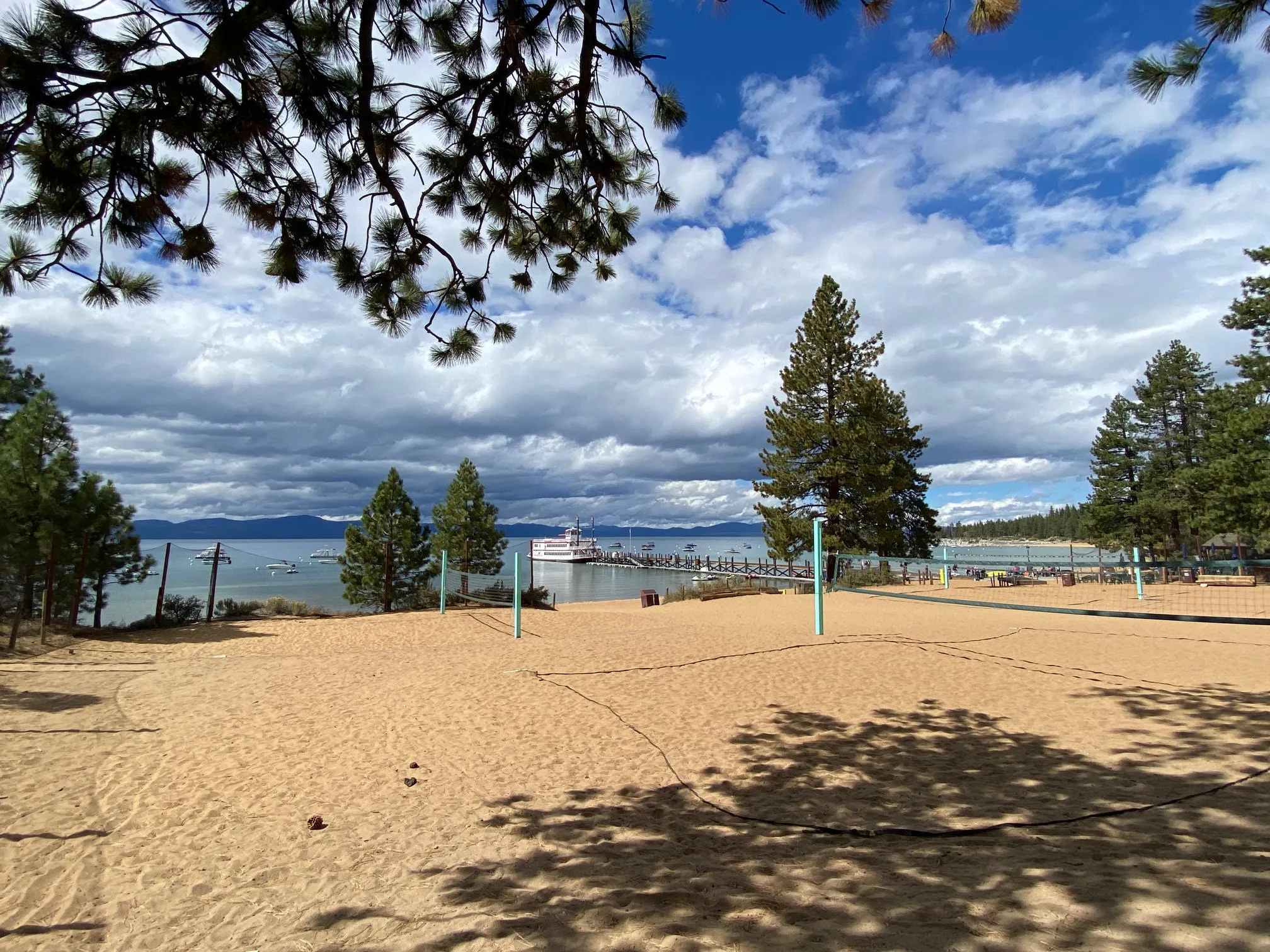 andy volleyball courts at Zephyr Cove Beach with pine trees, boats, and Lake Tahoe’s blue water in the background.