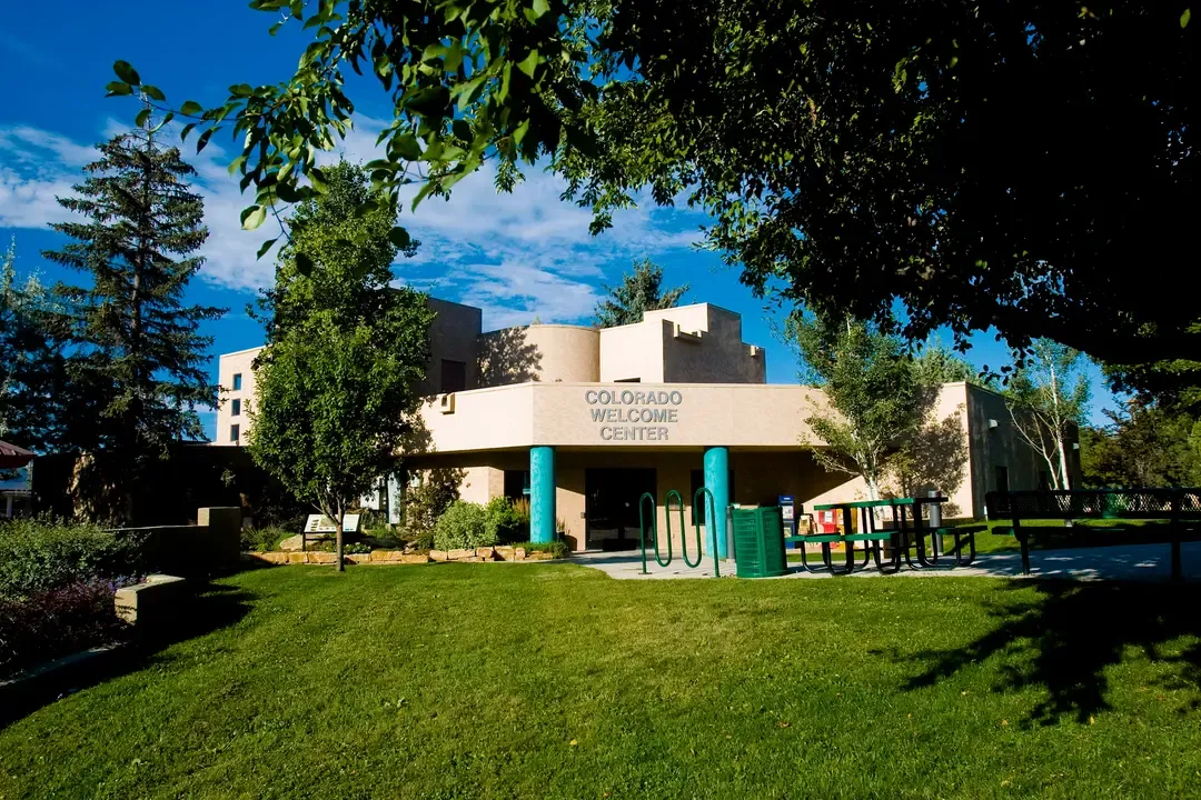 The Colorado Welcome Center in Cortez sits surrounded by trees and green lawn under a bright blue sky.
