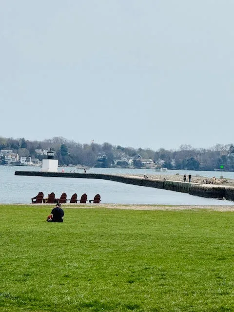 View of Derby Wharf in Salem, Massachusetts, featuring red Adirondack chairs, green lawn, and historic lighthouse.