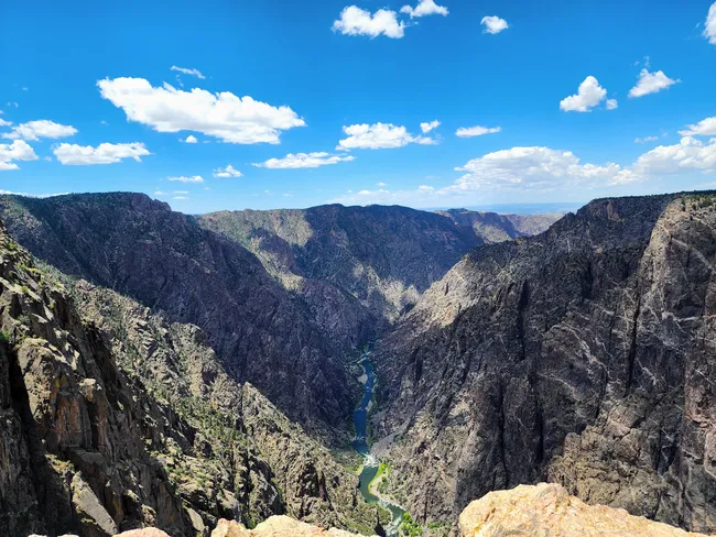 A clear blue sky stretches over the deep, rugged cliffs of Black Canyon, with the Gunnison River winding below.