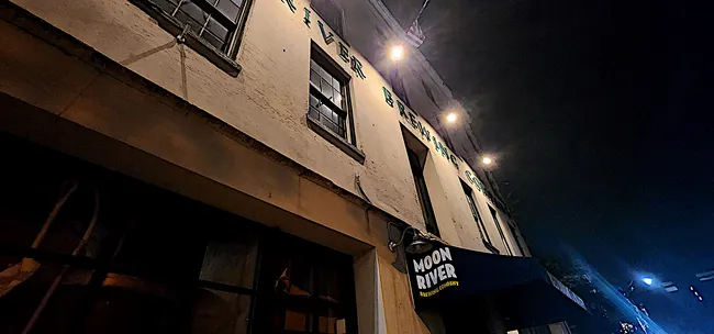 View of the Moon River Brewing building at night, showcasing dimly lit windows and a prominent awning.
