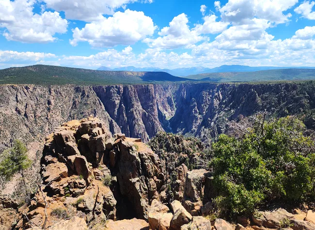 A dramatic view of Black Canyon under a bright blue sky with scattered clouds and rugged cliffs.