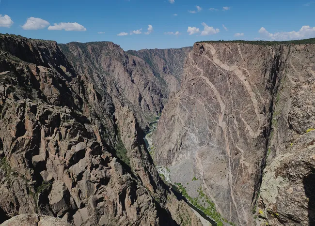 Sheer canyon walls tower over the winding Gunnison River at Black Canyon, highlighting the vertical drama and layered geology of the landscape.