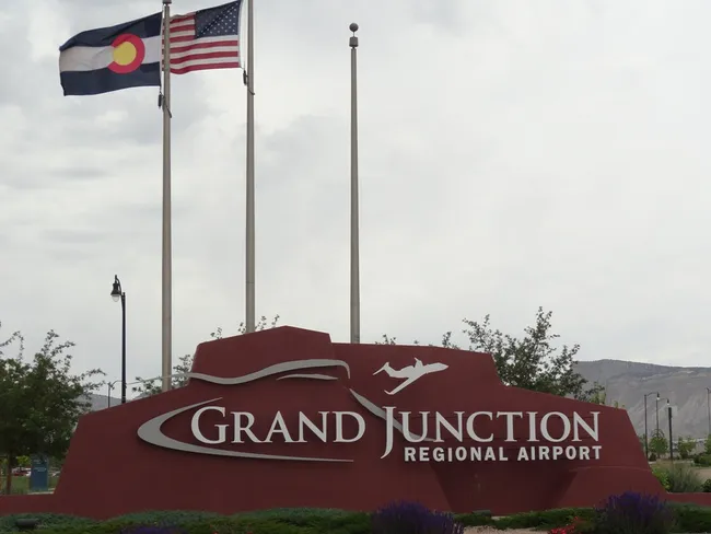 Entrance sign for Grand Junction Regional Airport with U.S. and Colorado state flags flying above.