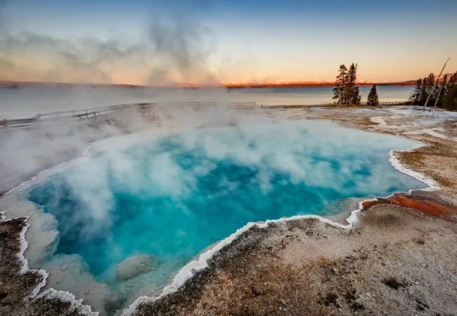 A steaming turquoise hot spring at West Thumb Geyser Basin glowing at sunrise in Yellowstone National Park.