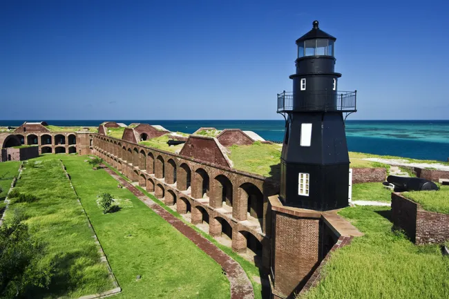The black Garden Key Lighthouse at Fort Jefferson, overlooking lush greenery and bright blue ocean views.