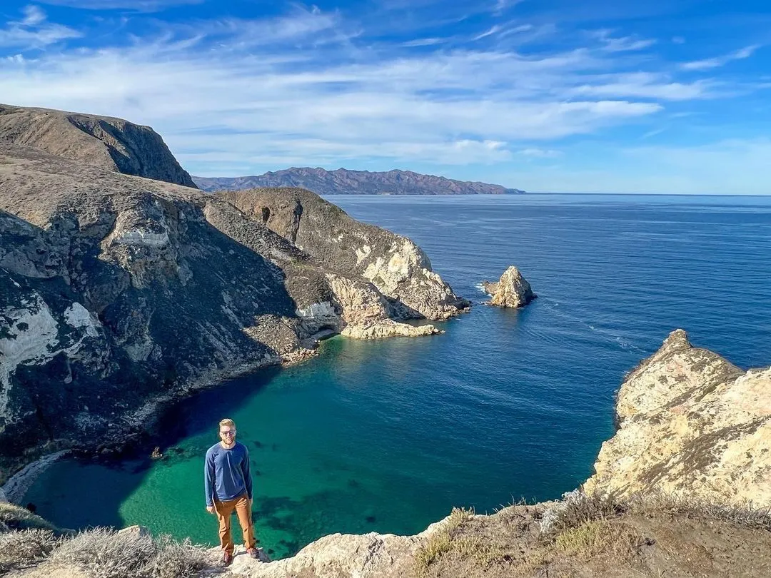 Man standing on a cliff overlooking a rugged coastline and turquoise cove at Channel Islands National Park.