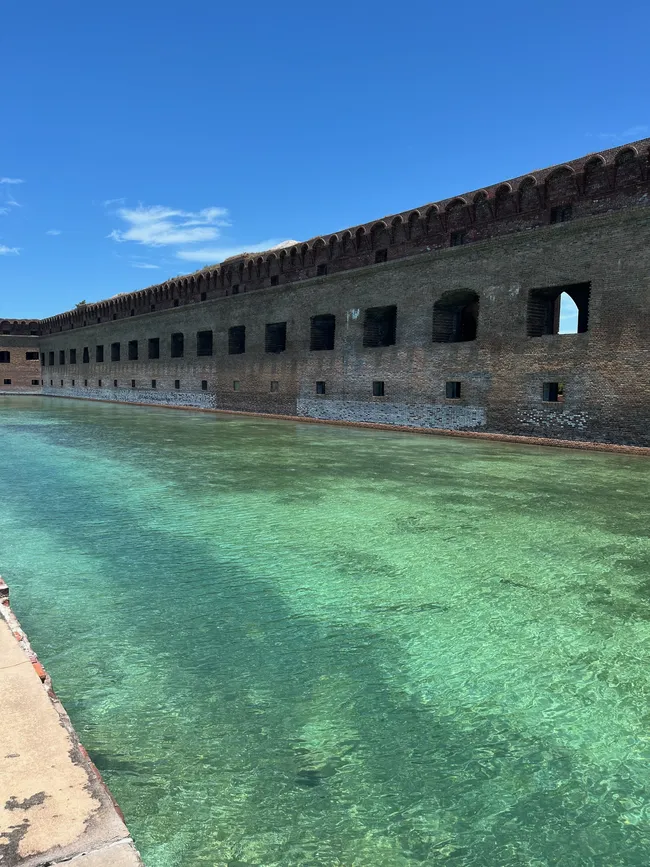 Clear turquoise waters surround the brick walls of Fort Jefferson at Dry Tortugas National Park under a bright blue sky.