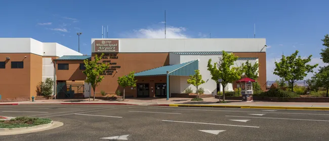 Exterior view of Canyonlands Regional Airport with a small terminal building, blue awnings, and clear desert skies.