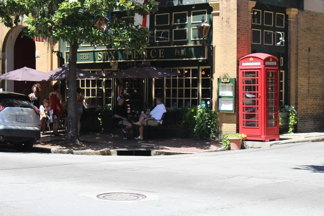 The Six Pence Pub with outdoor seating and a red telephone booth on a sunny street in Savannah.