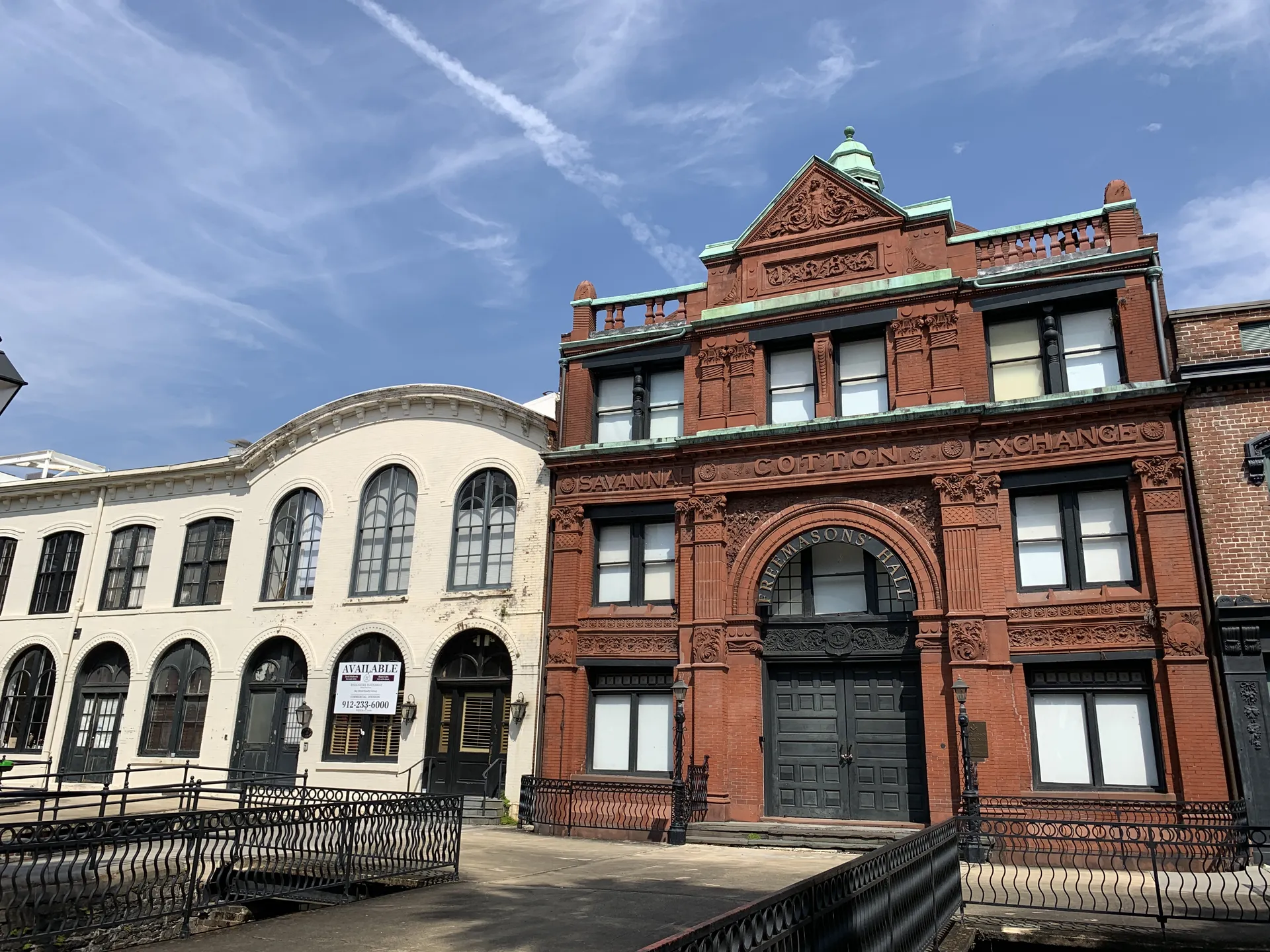 View of historic red-brick building with green accents, featuring arched windows and decorative elements, alongside a white curved structure.