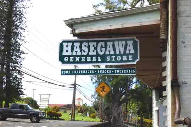 Sign for Hasegawa General Store hanging from a building, advertising food, beverages, snacks, and souvenirs.