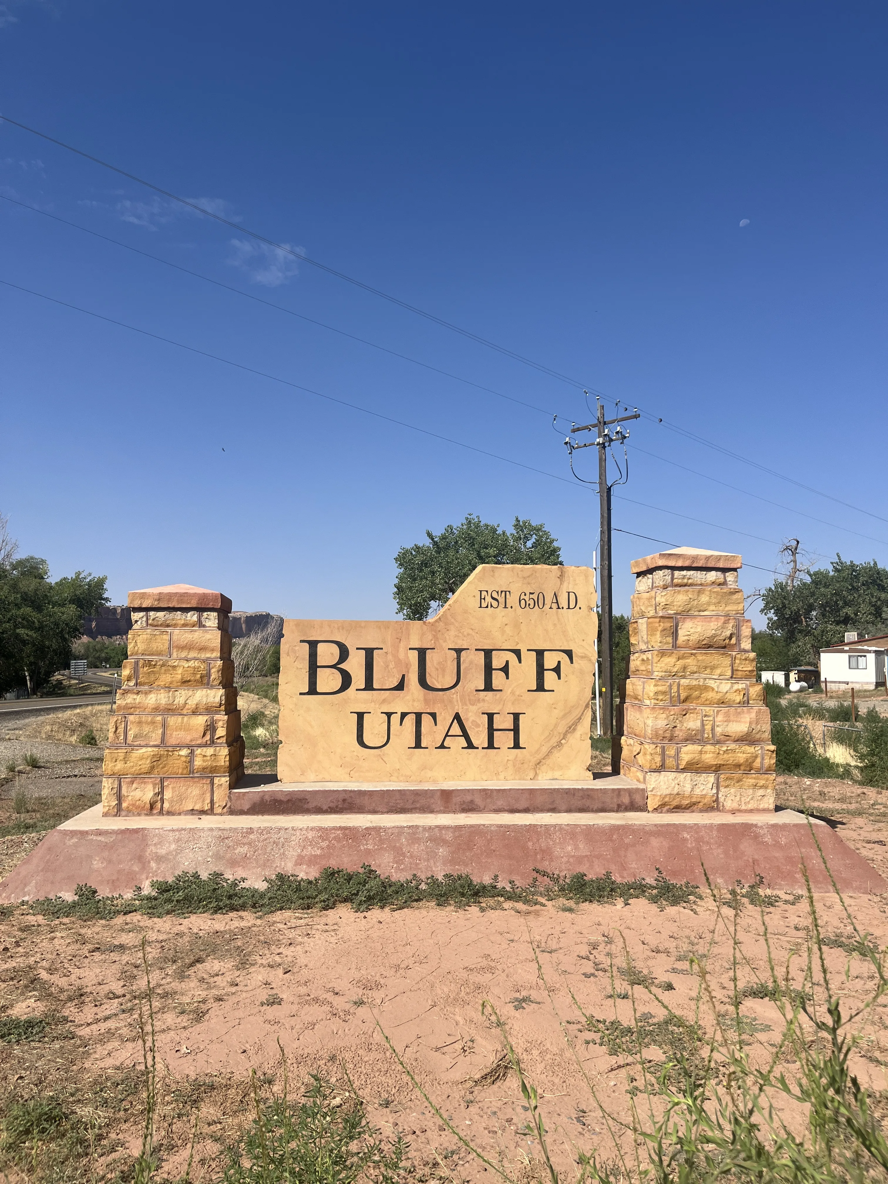 Stone monument sign welcomes visitors to Bluff, Utah, established in 650 A.D., with clear skies in the background.