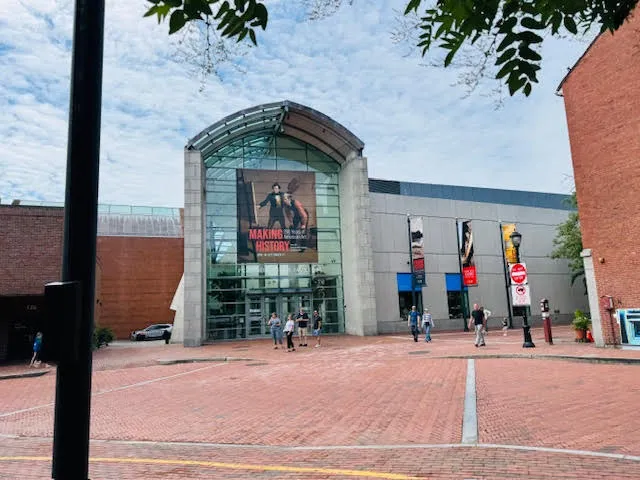 The glass-front entrance of the Peabody Essex Museum in Salem, Massachusetts, with visitors walking across a red brick plaza.