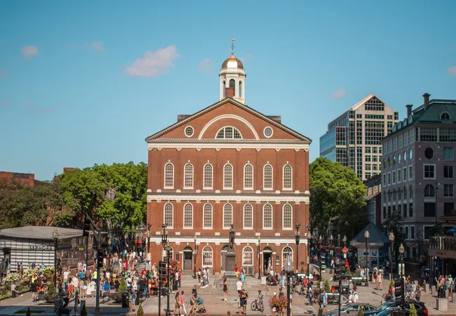 Crowds walk through the plaza in front of Boston’s historic Faneuil Hall, framed by shops and modern buildings.