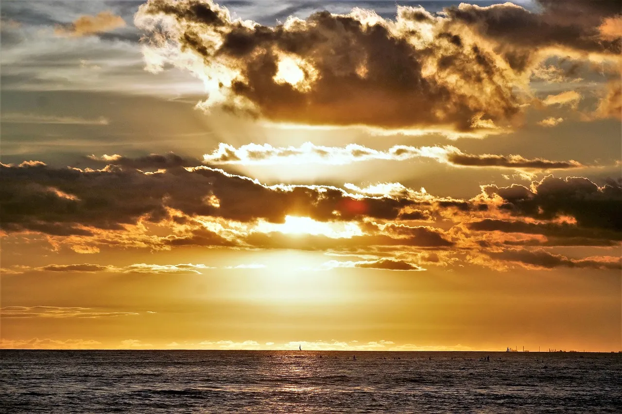 Golden sunset over the ocean with scattered clouds, casting dramatic light across the water and horizon.