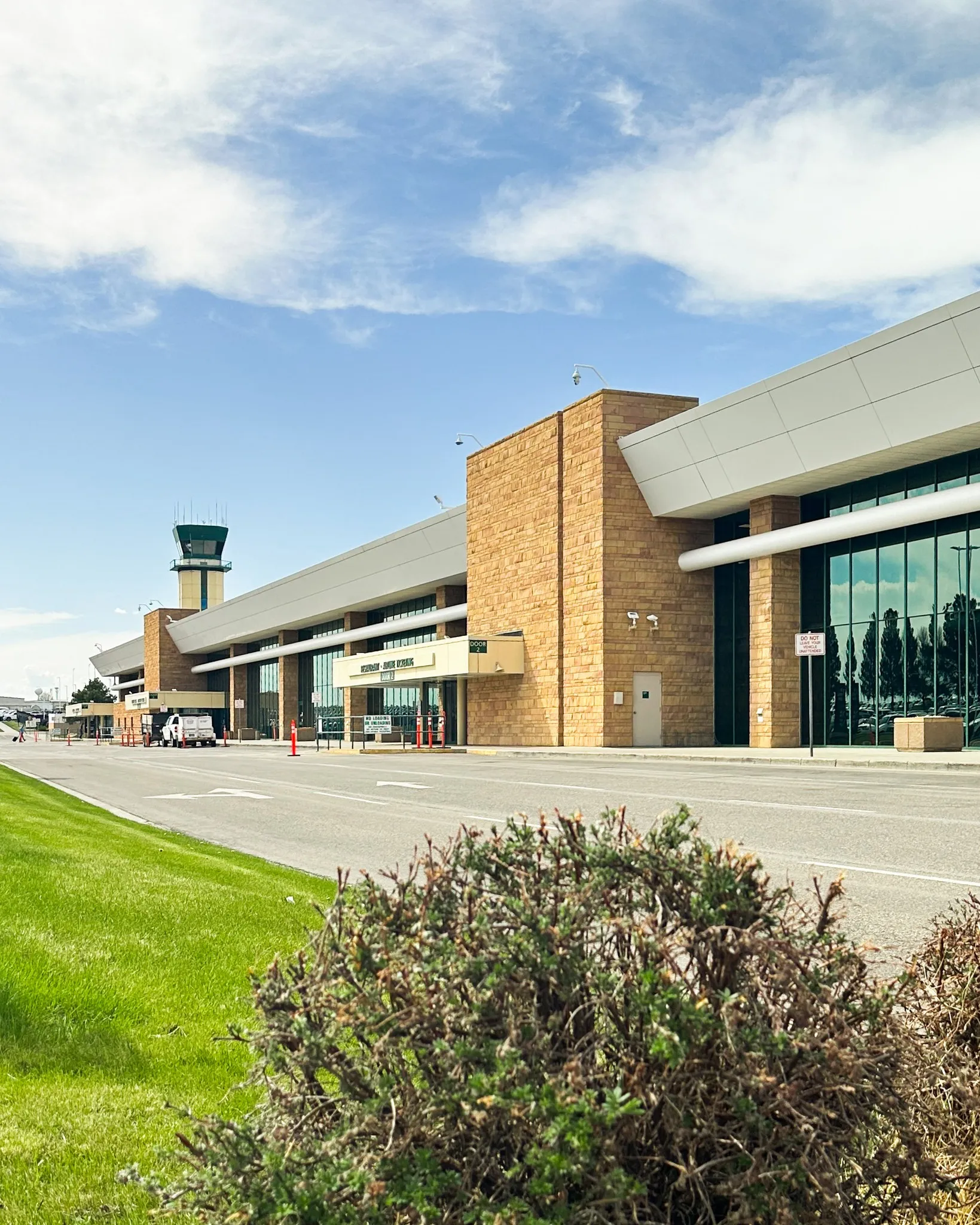 Modern airport terminal in Billings, Montana, with tan stone exterior, tall glass windows, and control tower in the background.