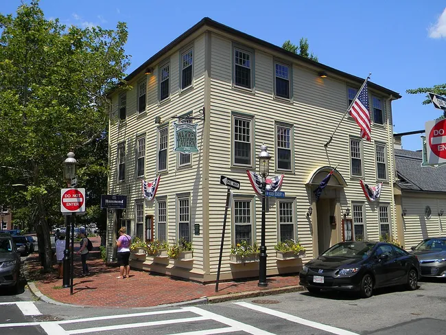 Historic three-story wooden building with American flags and flower boxes on a sunny street corner.