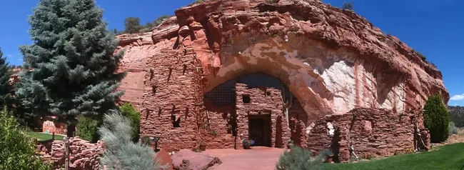 A group of people stand on a rocky hill overlooking a vast desert landscape layered with mesas and distant cliffs.