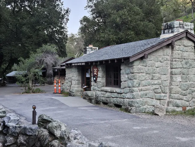 Stone National Park Service building at the Bear Gulch Nature Center, surrounded by trees and natural landscaping, with a paved walkway leading to the entrance.