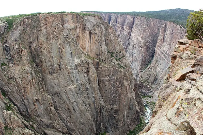 Steep, sheer cliffs of Black Canyon rise dramatically above the narrow river far below, showcasing rugged rock walls and deep vertical drops.