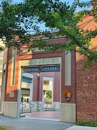Brick entrance of the Salem Armory Visitor Center framed by a leafy tree branch on a sunny day.
